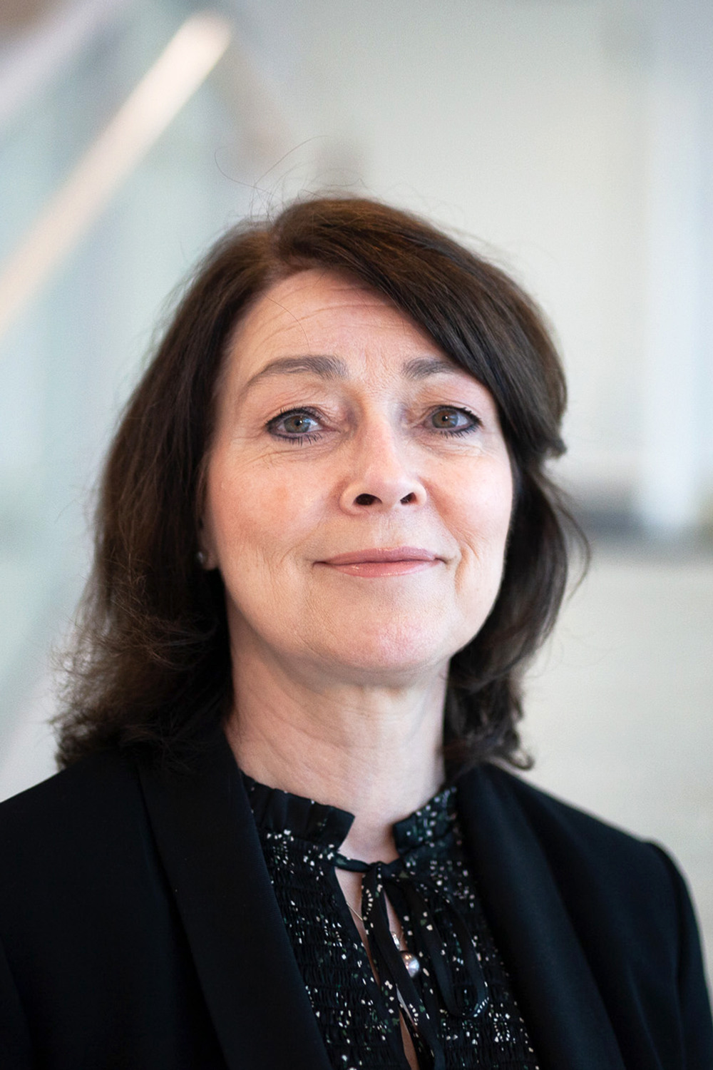 Kvinna i en glittrig blus med en svart kavaj över ståendes i ett fint ljust trapphus. 