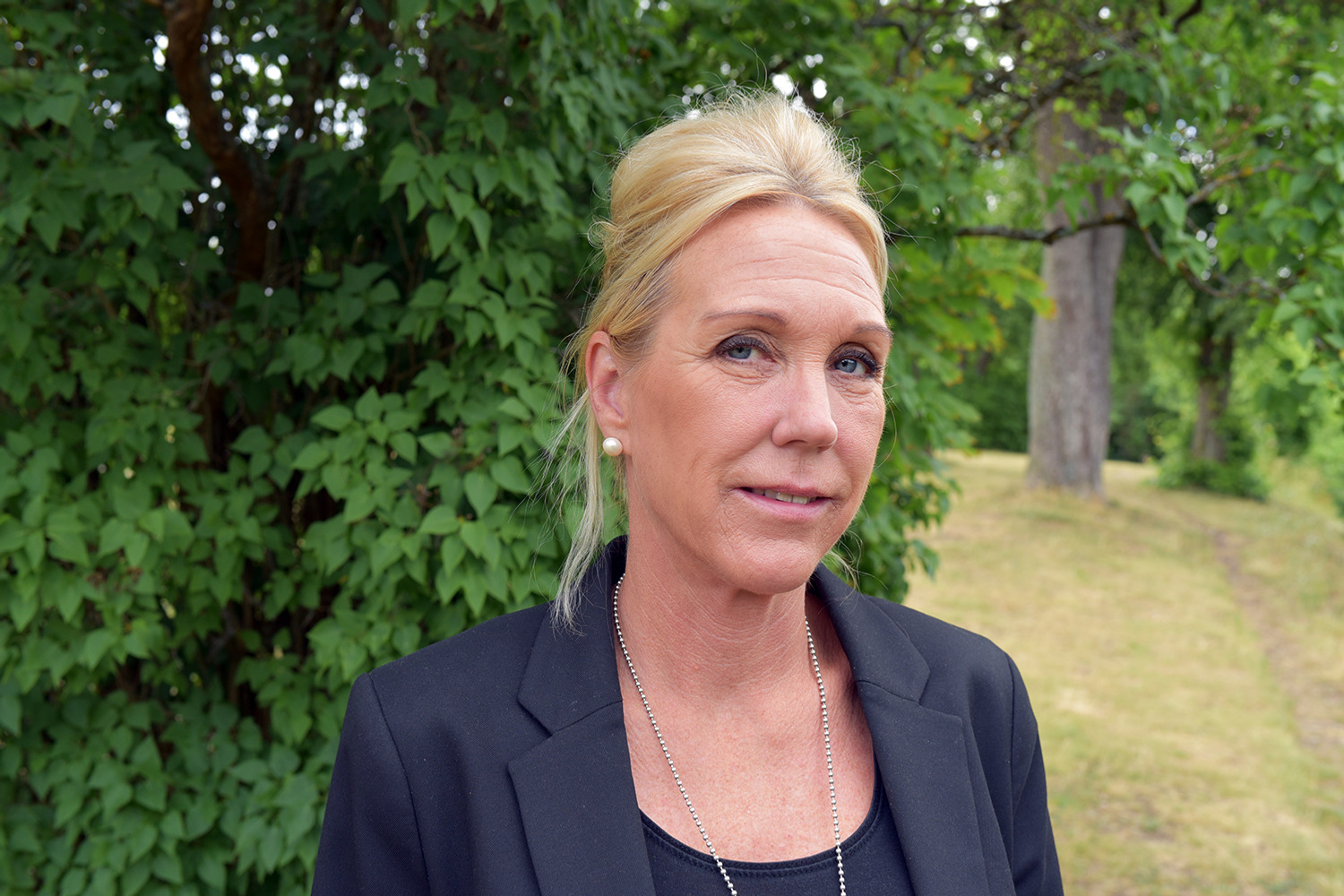 Kvinna i svart kavaj ståendes ute i naturen.