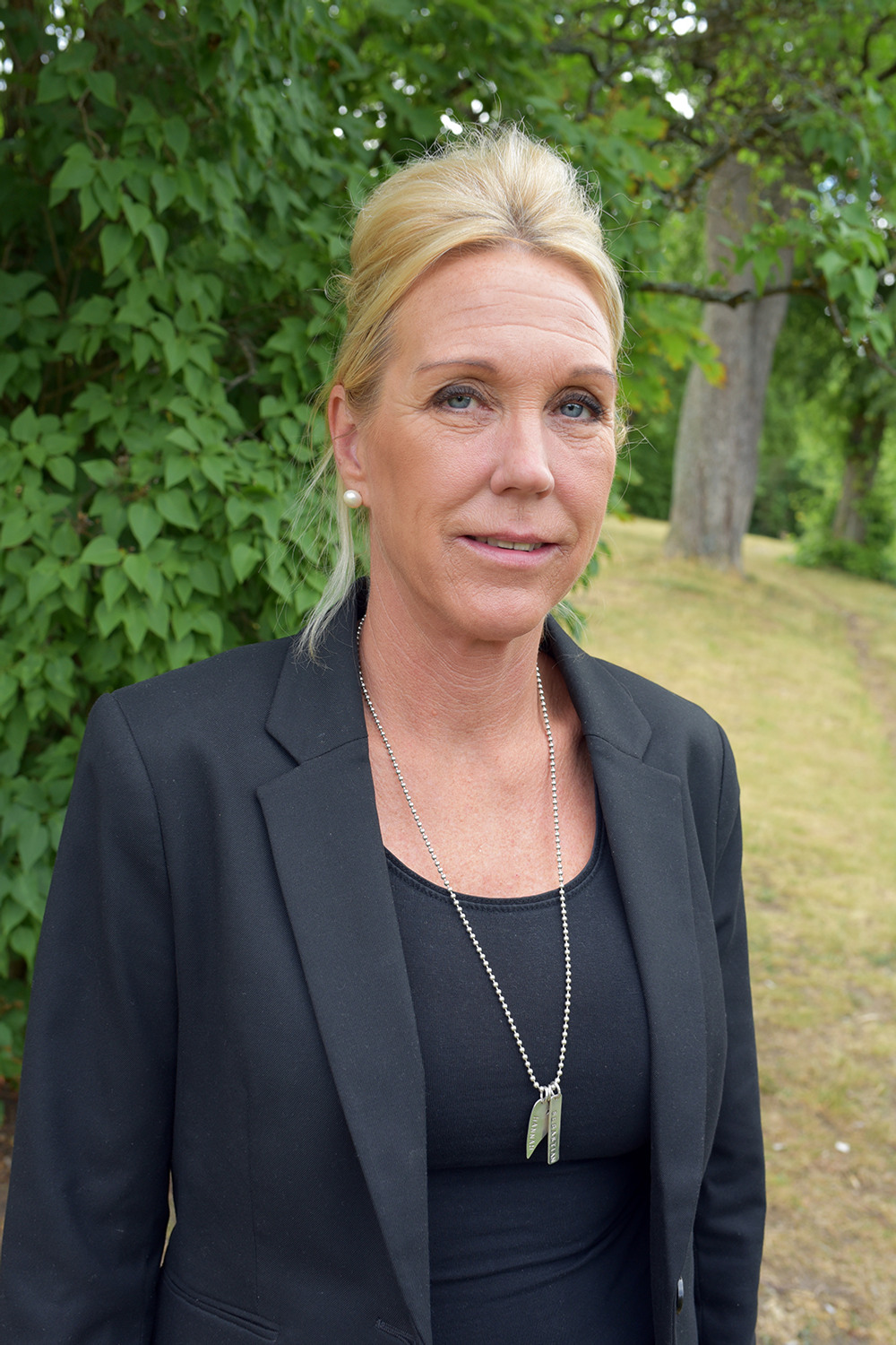 Kvinna i svart kavaj ståendes ute i naturen.