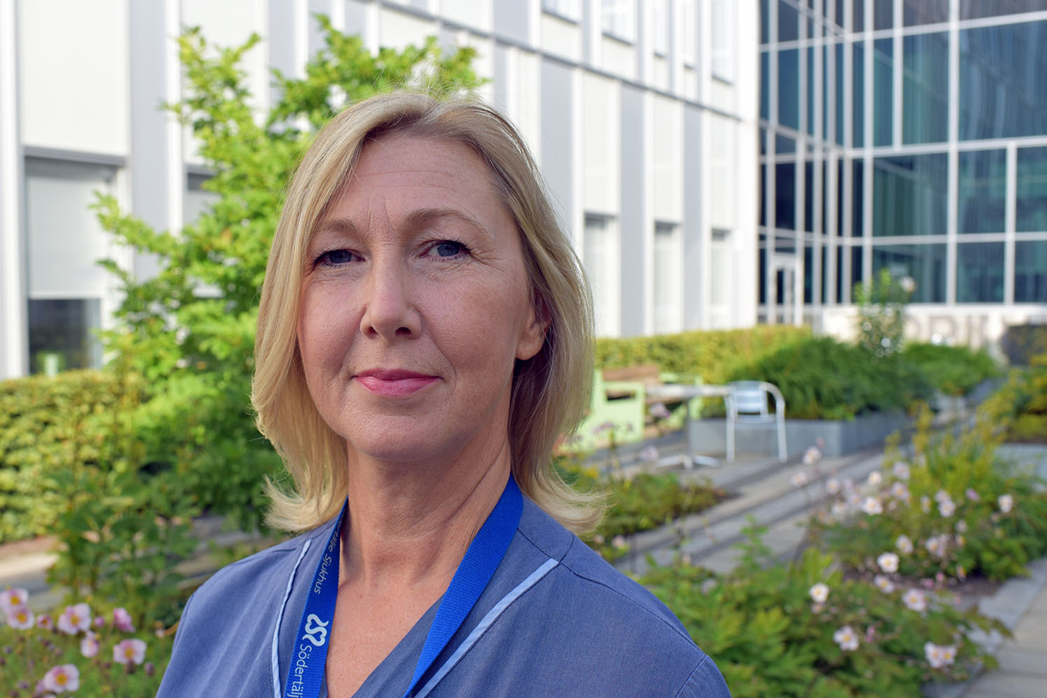 Kvinna ståendes på Södertälje sjukhus soliga innegård iklädd vårdkläder.