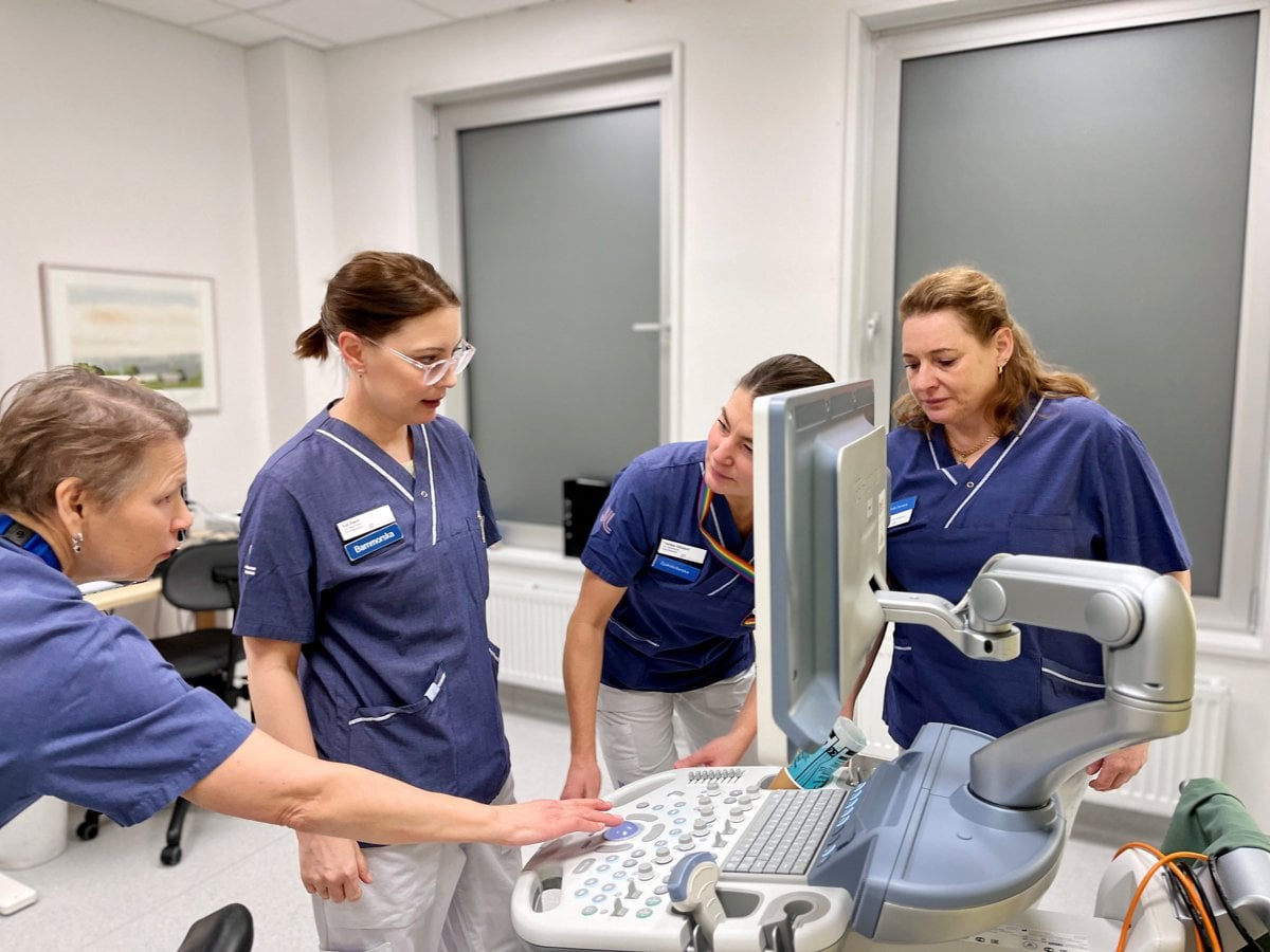 En grupp i blåa vårdkläder som står runt en dator