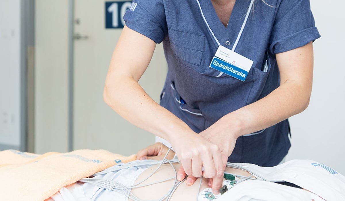 En kvinna i vårdkläder sätter på EKG på en patient i en säng