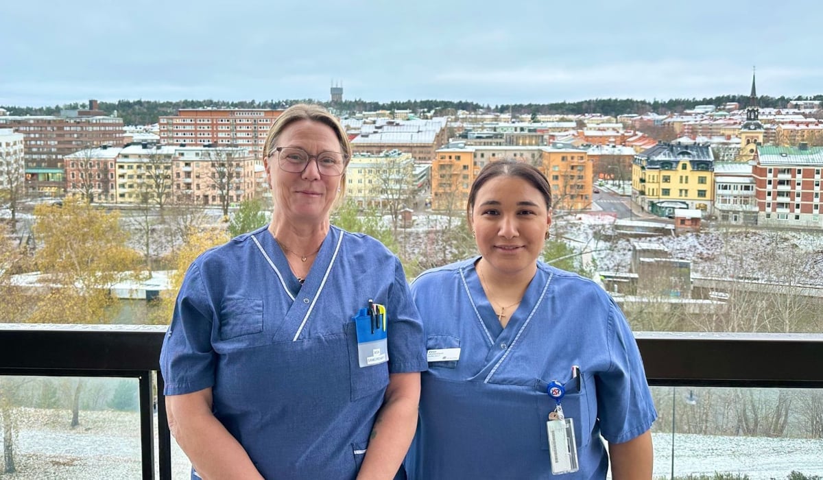 Två kvinnor står på en balkong. Stadskärna i bakgrunden.