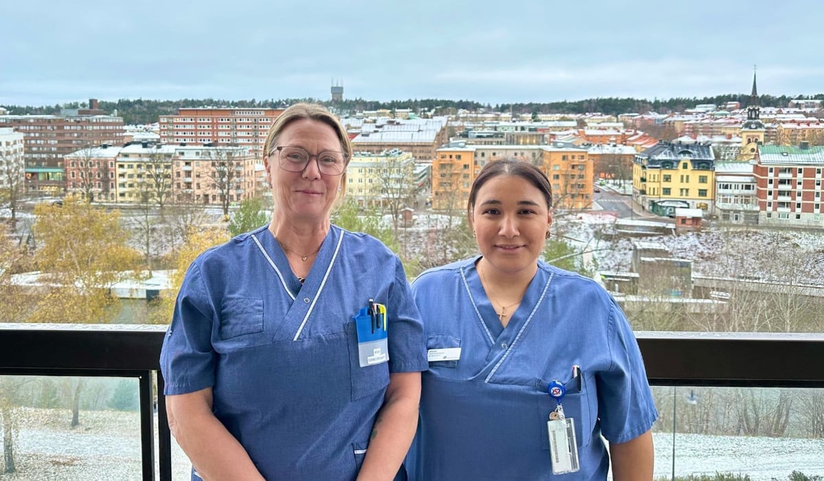 Två kvinnor står på en balkong. Stadskärna i bakgrunden.