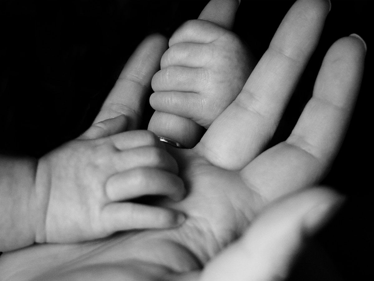 En bebis som håller i en vuxens hand i svartvit.