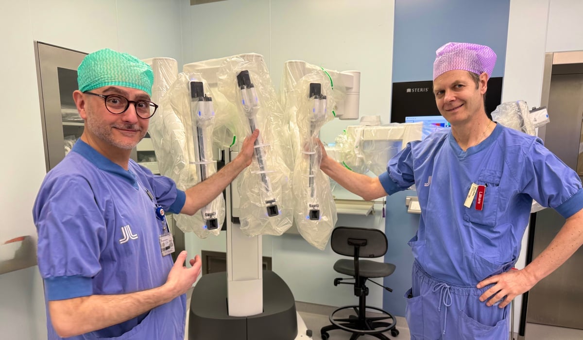 Två leende män i operationskläder står vid en operationsrobot
