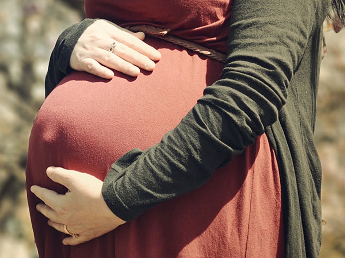 Kvinna som håller i sin gravidmage medan hon står ute i naturen.