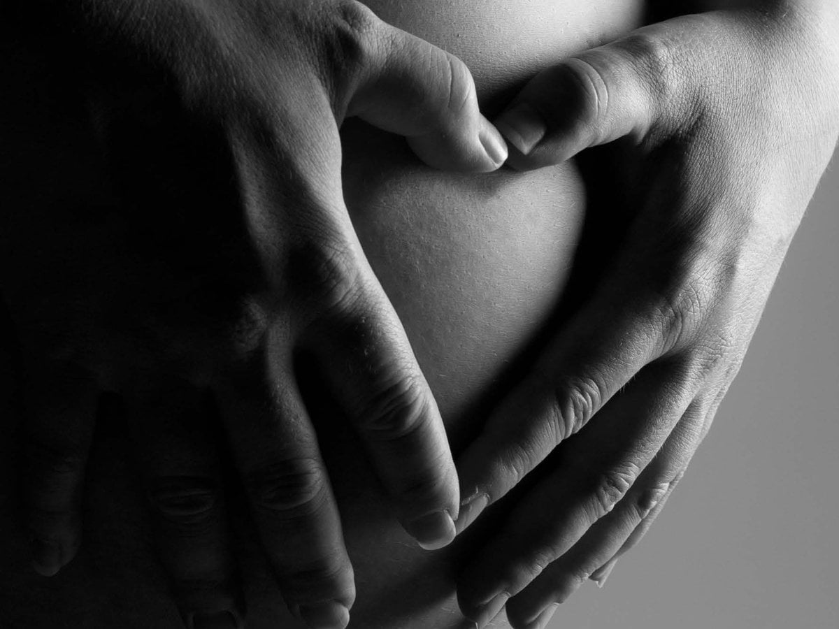 Händer som formar ett hjärta på en gravidmage.