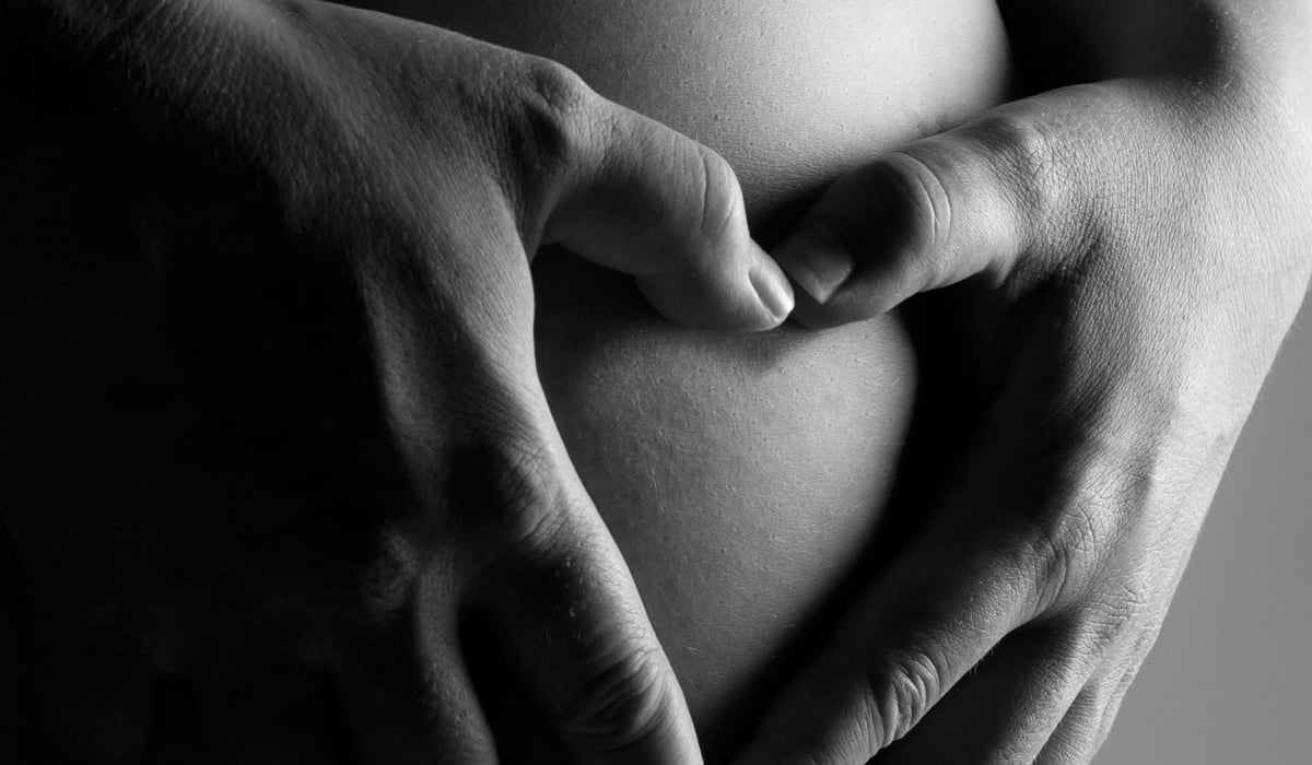 Händer som formar ett hjärta på en gravidmage.