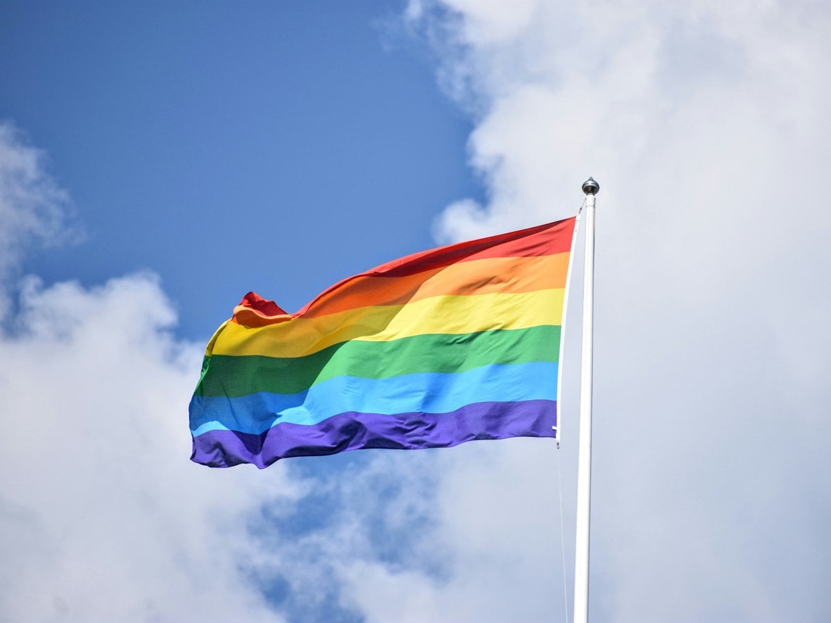 En regnbågsflagga som vajar på en flaggstång med himlen som bakgrund
