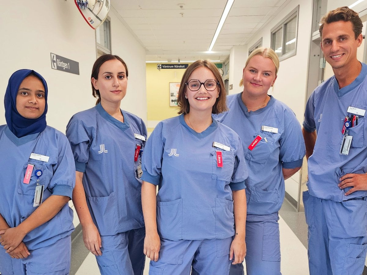 Leende läkare i vårdkläder poserar i en sjukhuskorridor