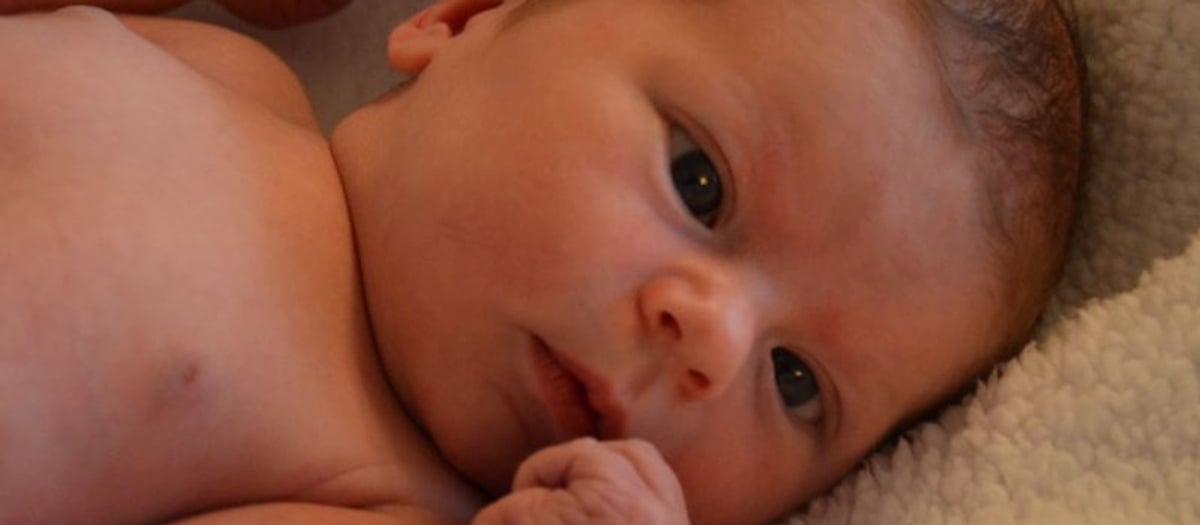 Bebis som ligger i en mysig vit teddyfilt och kollar med stora ögon.