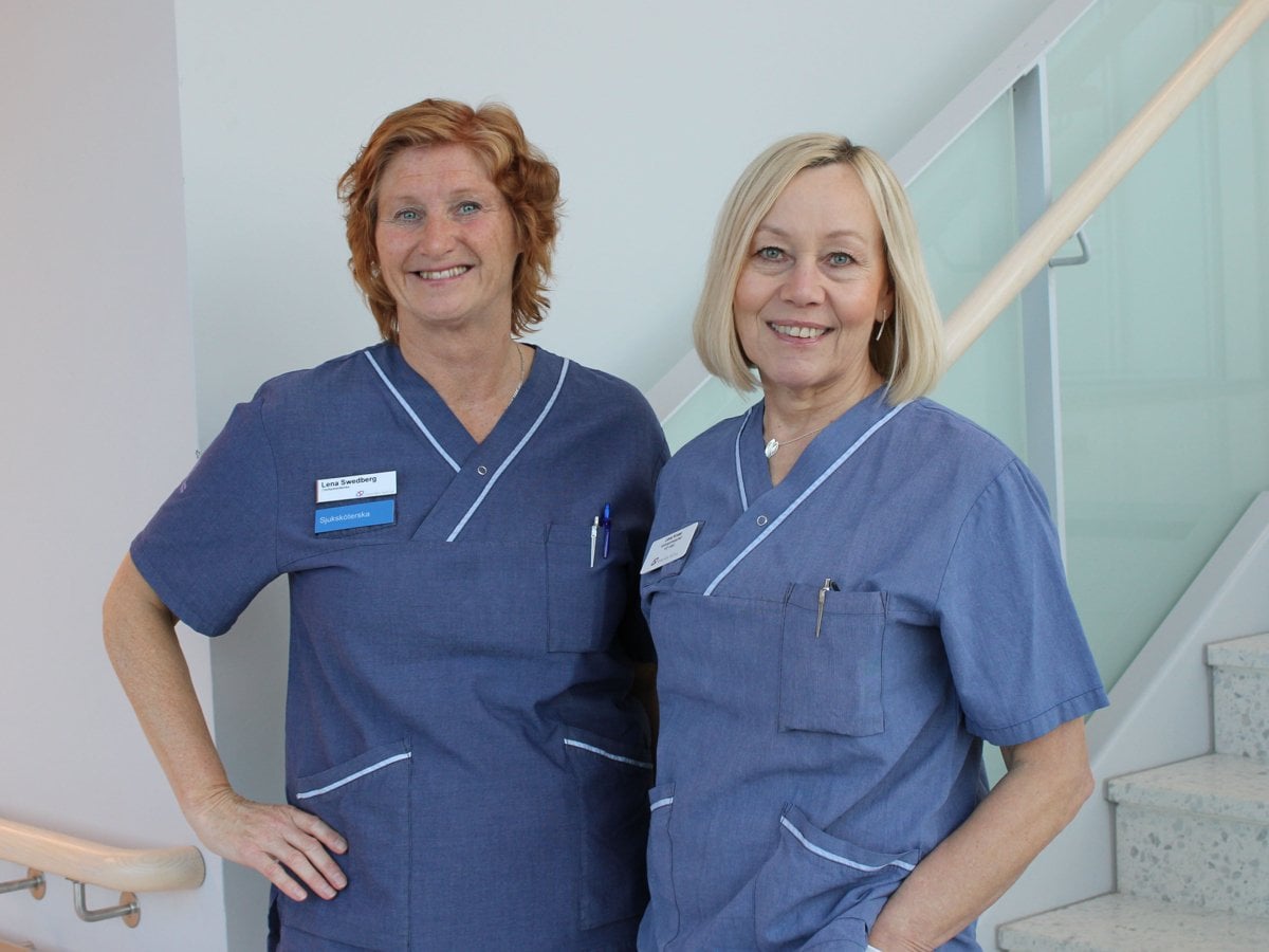 Två kvinnor ståendes i ett trapphus iklädda blåa vådklläder leendes mot kameran.