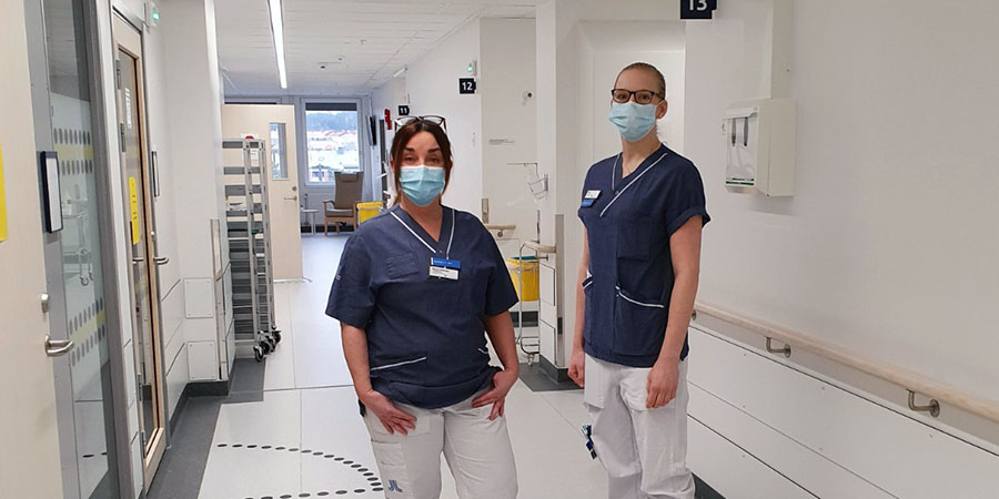Två medarbetare med munskydd står i sjukhuskorridor