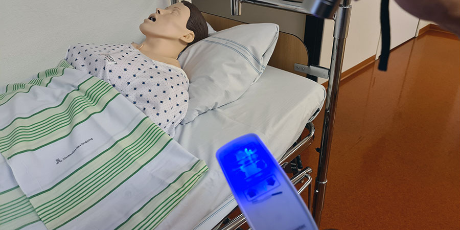 UV-ljus på en fjärrkontroll visar att smuts finns kvar. I bakgrunden en patientdocka i sjukhussäng.