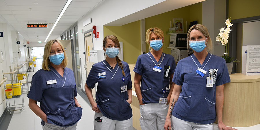 Fyra medarbetare i munskydd står i en sjukhuskorridor