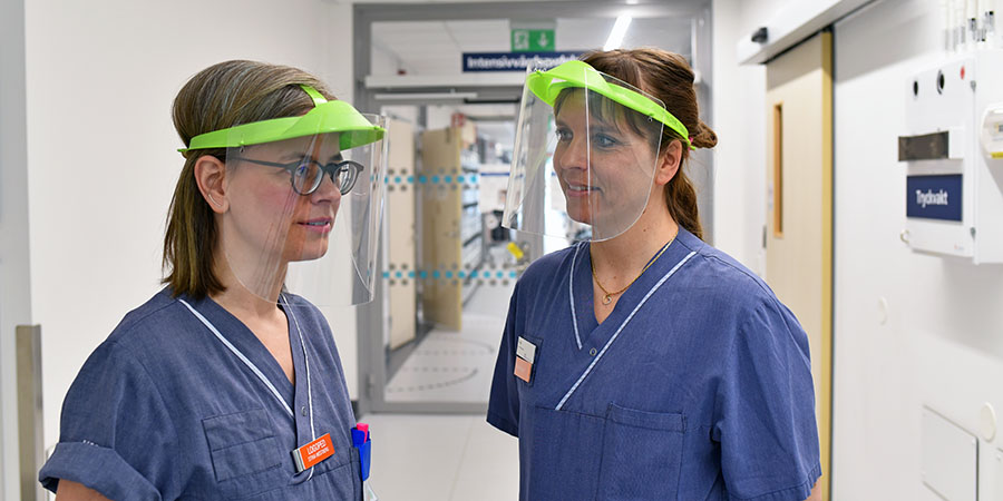 Två medarbetare i sjukhuskläder och visir står i sjukhuskorridor